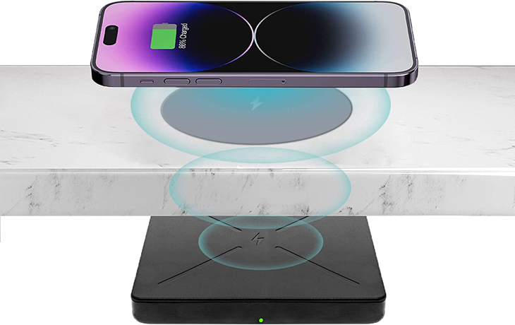 Diagram: a phone charging on top of a worktop, with the InvisaCharge unit fixed underneath the worktop