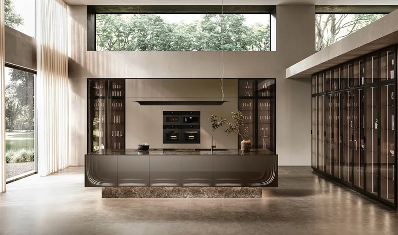 Febal Casa ONDA island with curved end in bronze finish, on a stone plinth, with tall glass-door units in the background